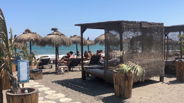 Eine Strandlounge mit Reetdachschirmen, Liegestühlen und einer Holzpergola.