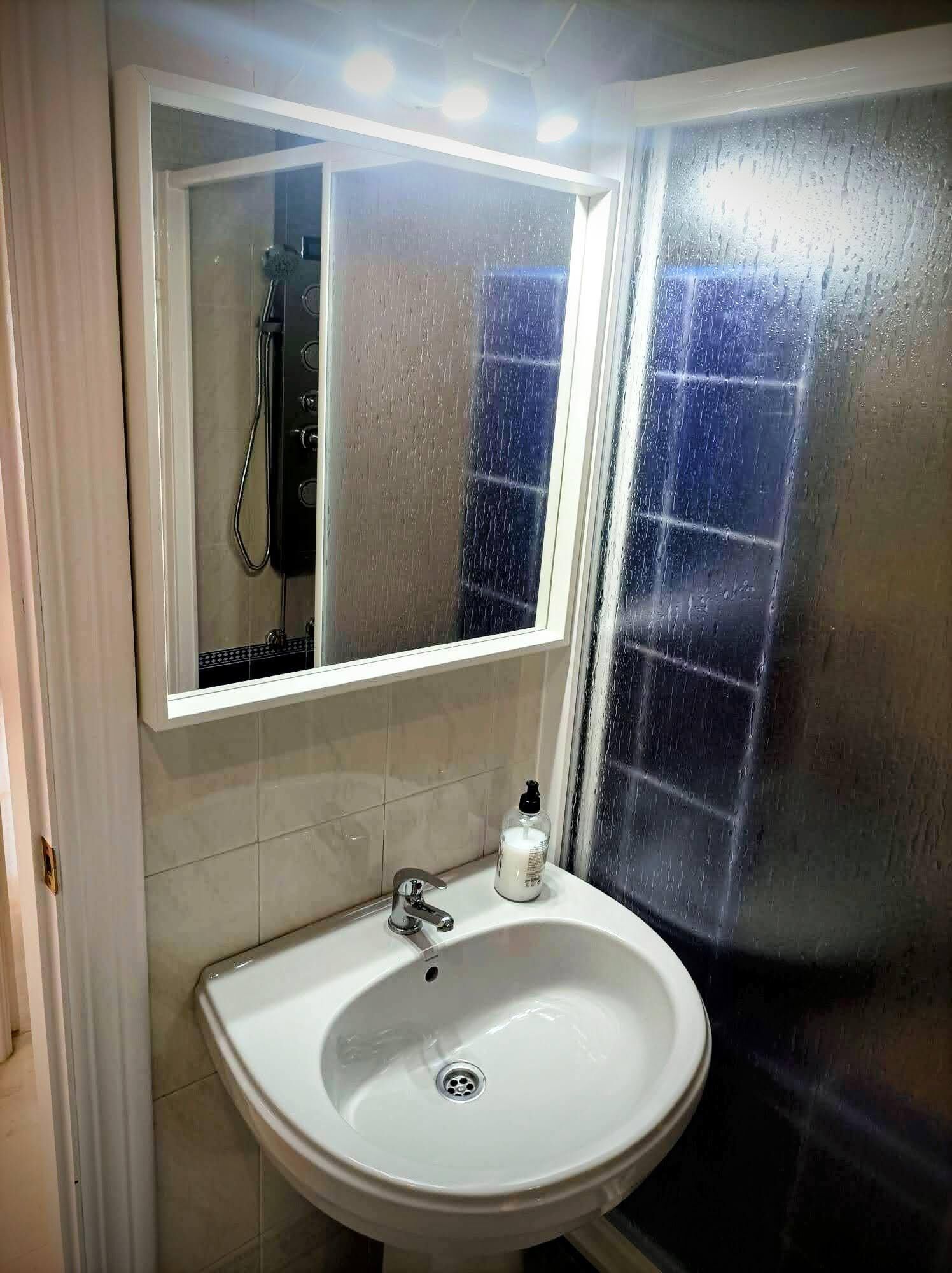 Een badkamer met een witte wastafel, een spiegel en een douche.