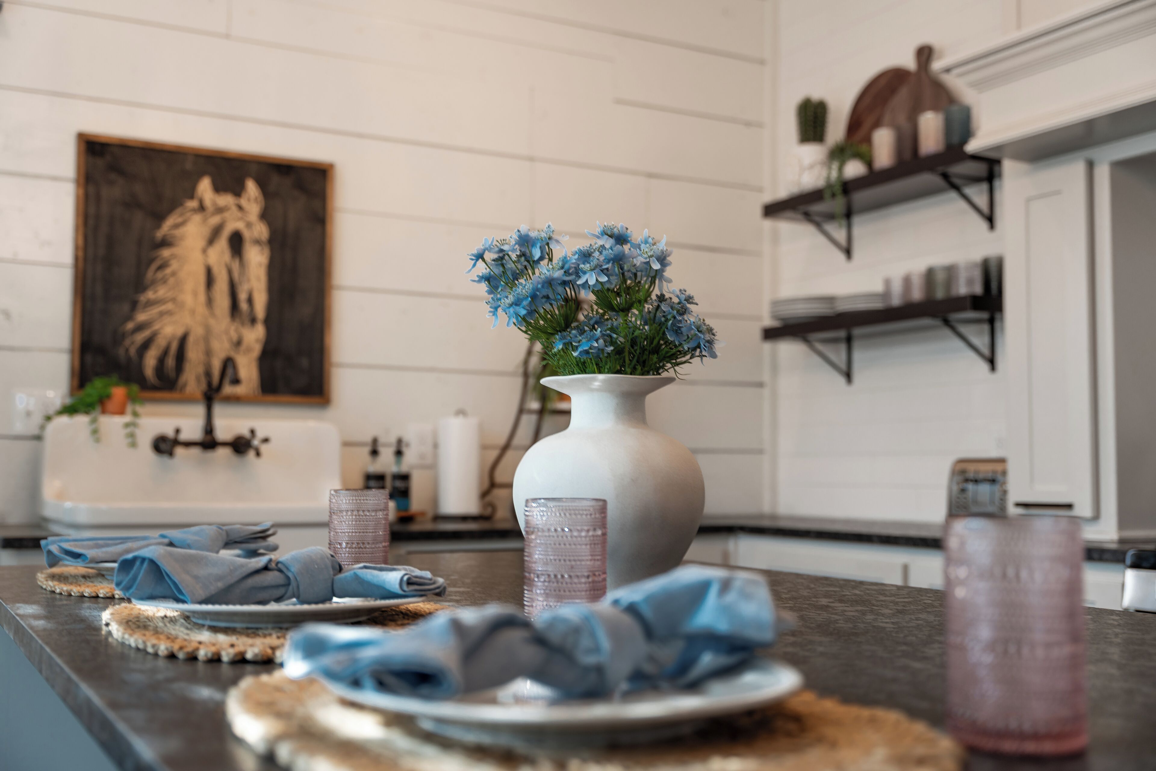 A kitchen counter with a vase of flowers, a toaster, and a painting on the wall.
