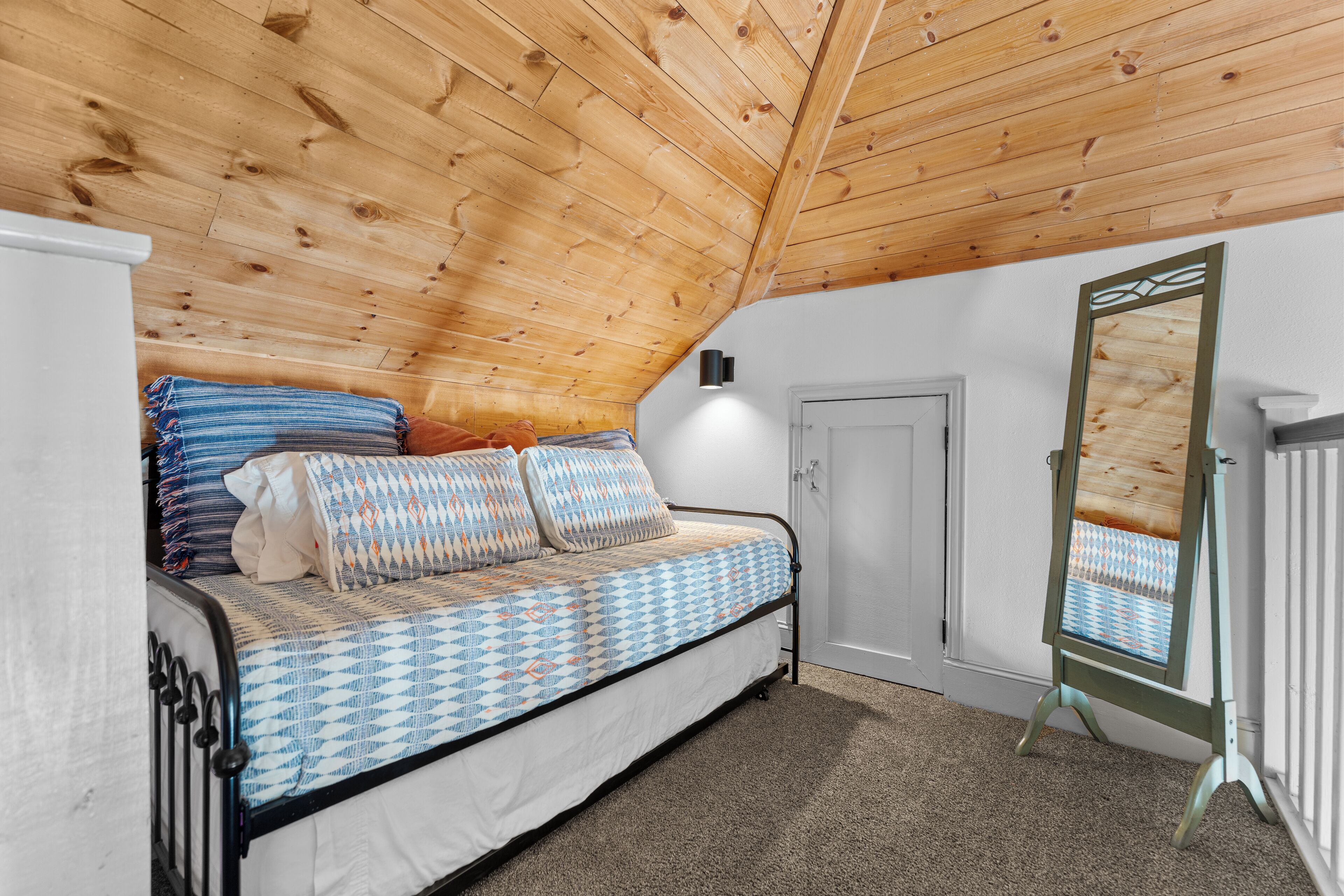A bedroom with a wooden ceiling, a bed with patterned bedding, a mirror, and a door.