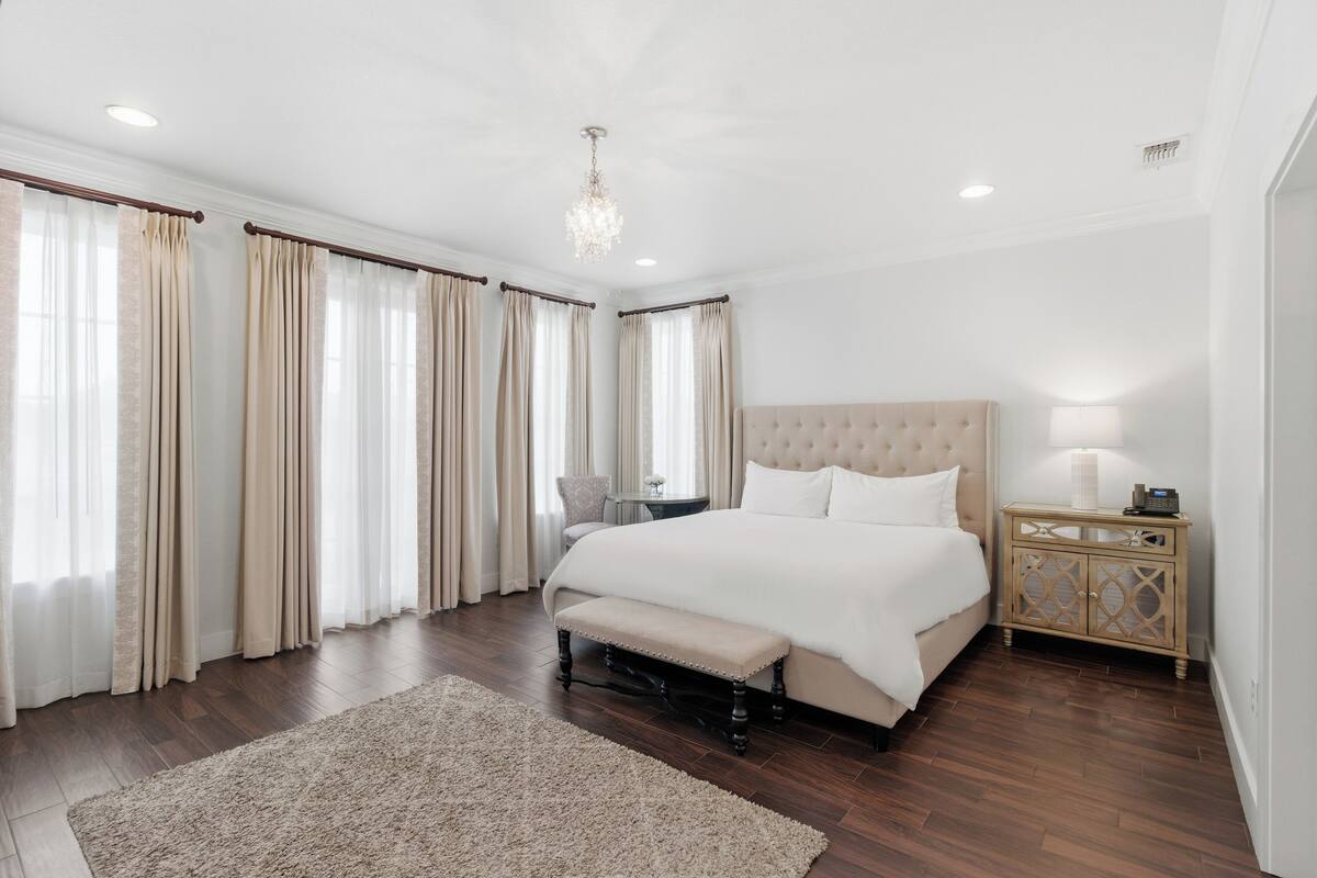 A bedroom with a large bed, a bench, a bedside table, and a chandelier.