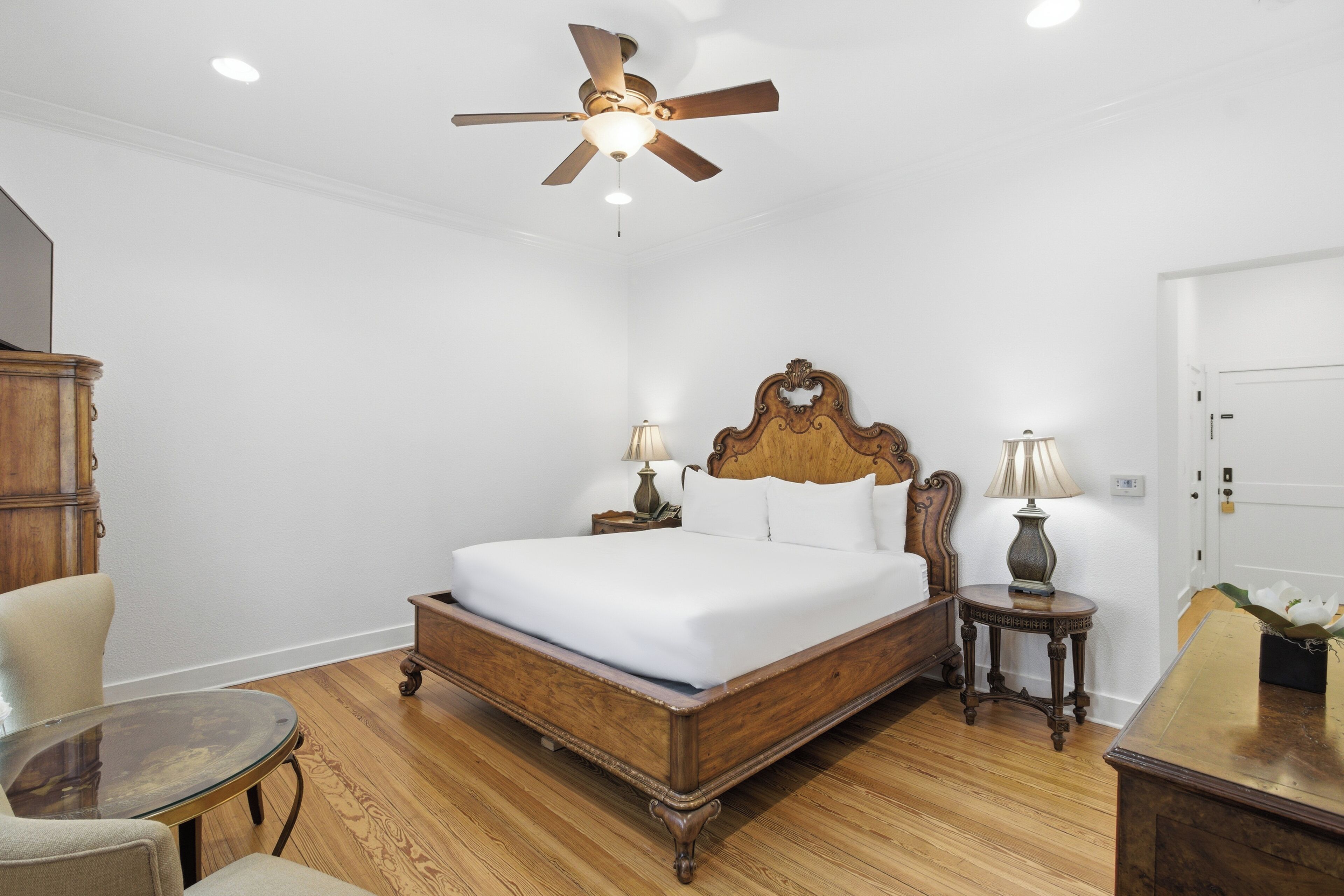 Ein Schlafzimmer mit einem Holzbett, zwei Nachttischen mit Lampen, einem Deckenventilator und Holzboden.