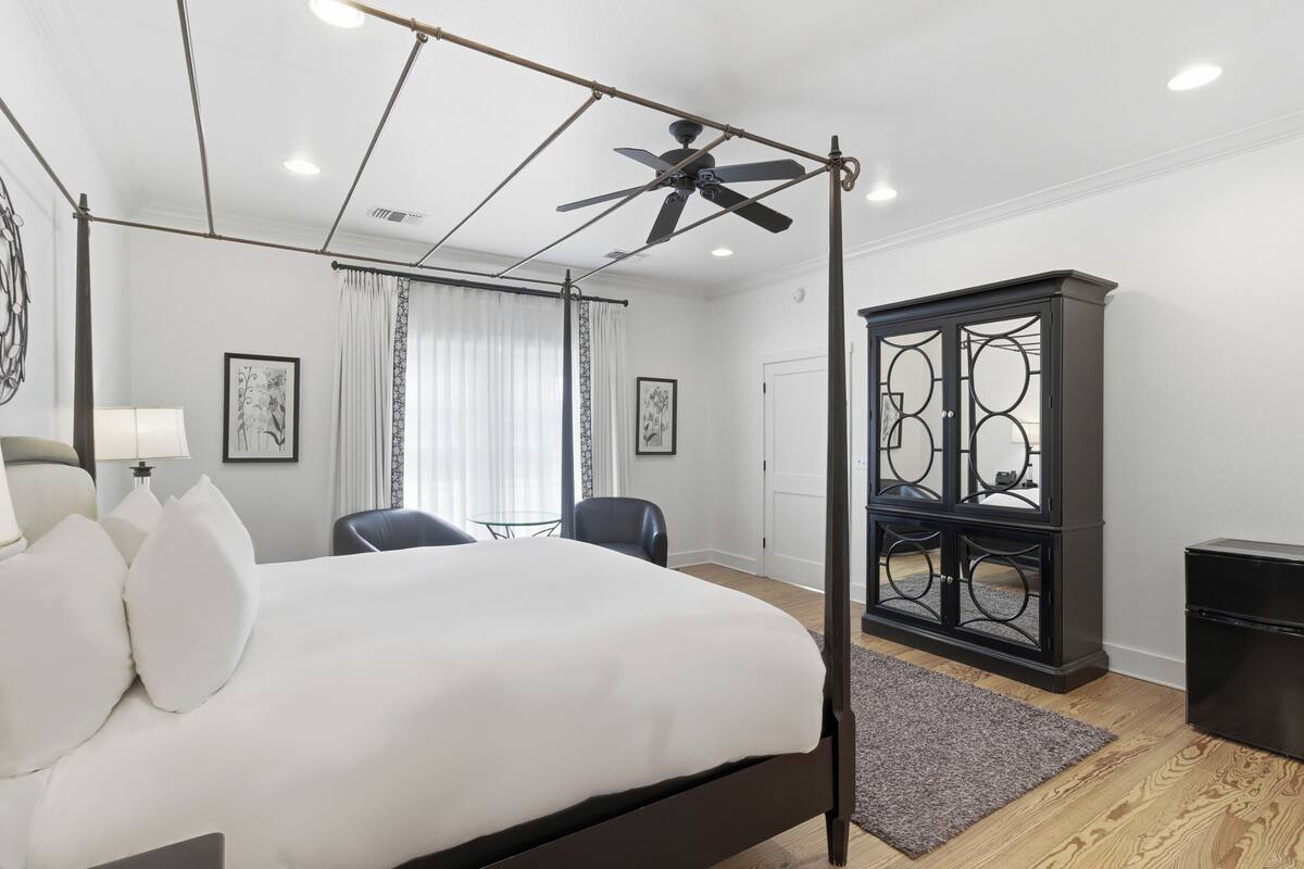 A bedroom with a bed, a ceiling fan, a desk, a chair, and a cabinet.
