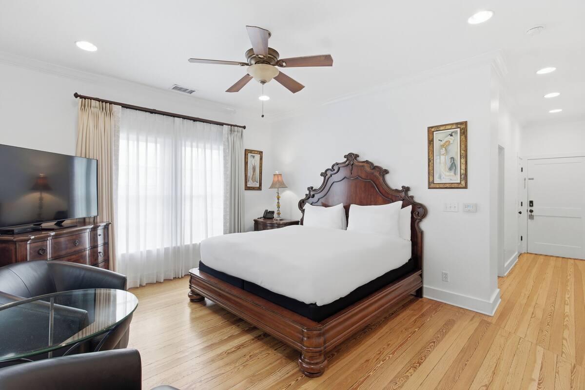 A hotel room with a wooden bed, a television, a glass table, and a ceiling fan.