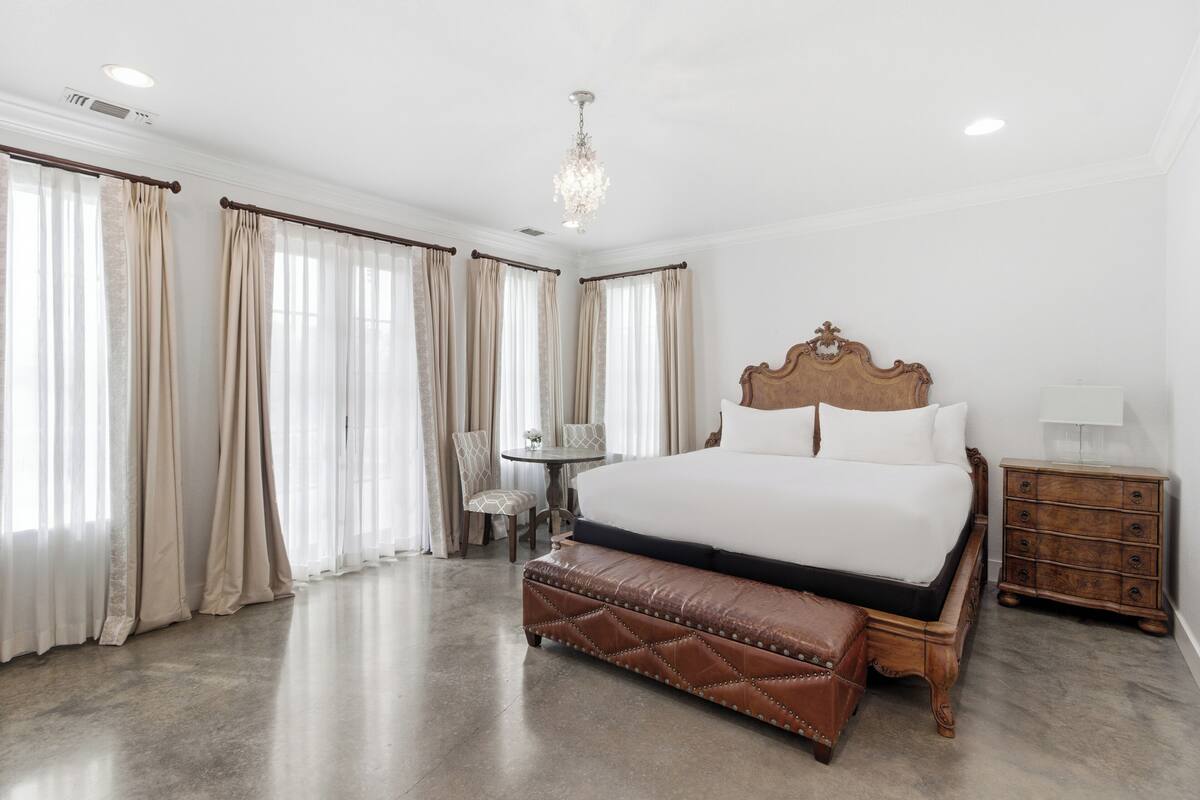 A spacious bedroom with a large bed, a wooden nightstand, a bench, and a small table with chairs.