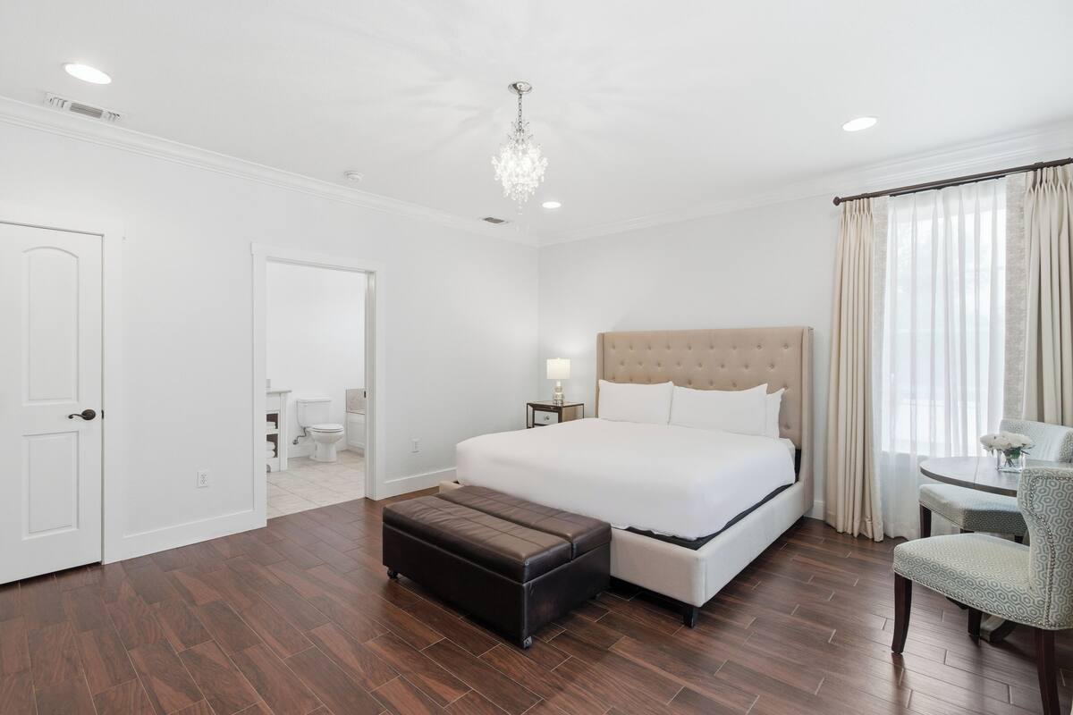 A hotel room with a large bed, a bedside table, a chair, and a wooden floor.