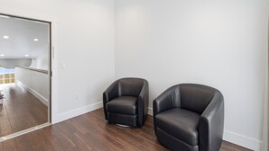 A room with two black leather chairs, wooden flooring, white walls, and a glass door leading to another room. - Emigrant's Inn (Fredericksburg)