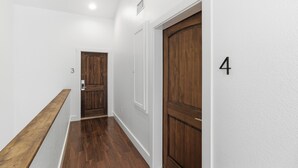 A hallway with wooden flooring, white walls, and a door marked with the number 4. - Emigrant's Inn (Fredericksburg)