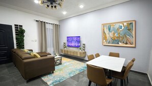 Una sala de estar moderna con un sofá, una mesa de comedor, sillas, un televisor y obras de arte en la pared.