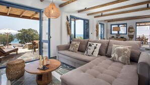 A modern living room with a sofa, a round wooden table, and a view of the sea through large windows.
