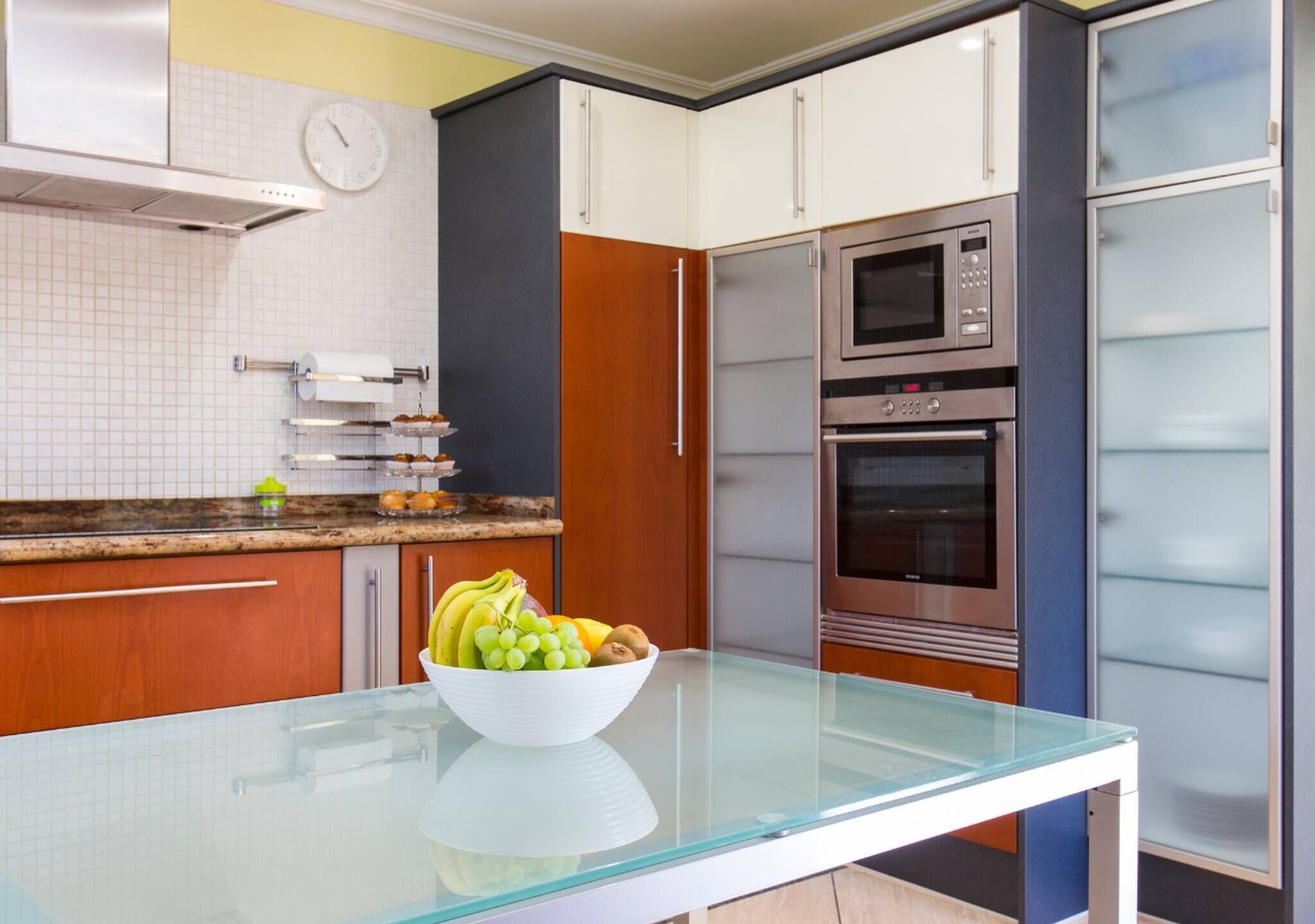 A modern kitchen with a glass-top table, stainless steel appliances, and wooden cabinets.