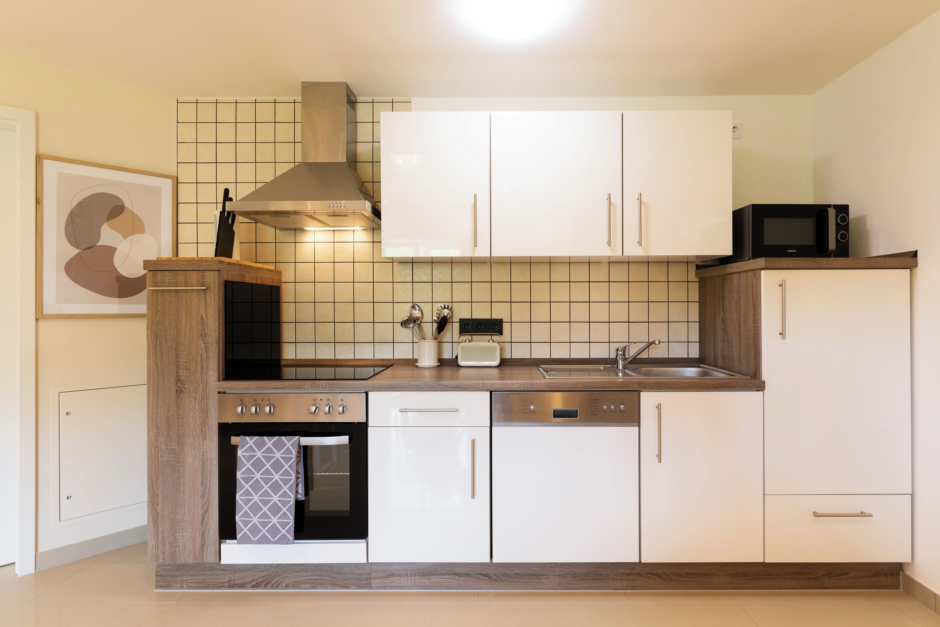 Eine moderne Küche mit weißen Schränken, einem eingebauten Backofen, einer Mikrowelle und einer Edelstahl-Dunstabzugshaube.