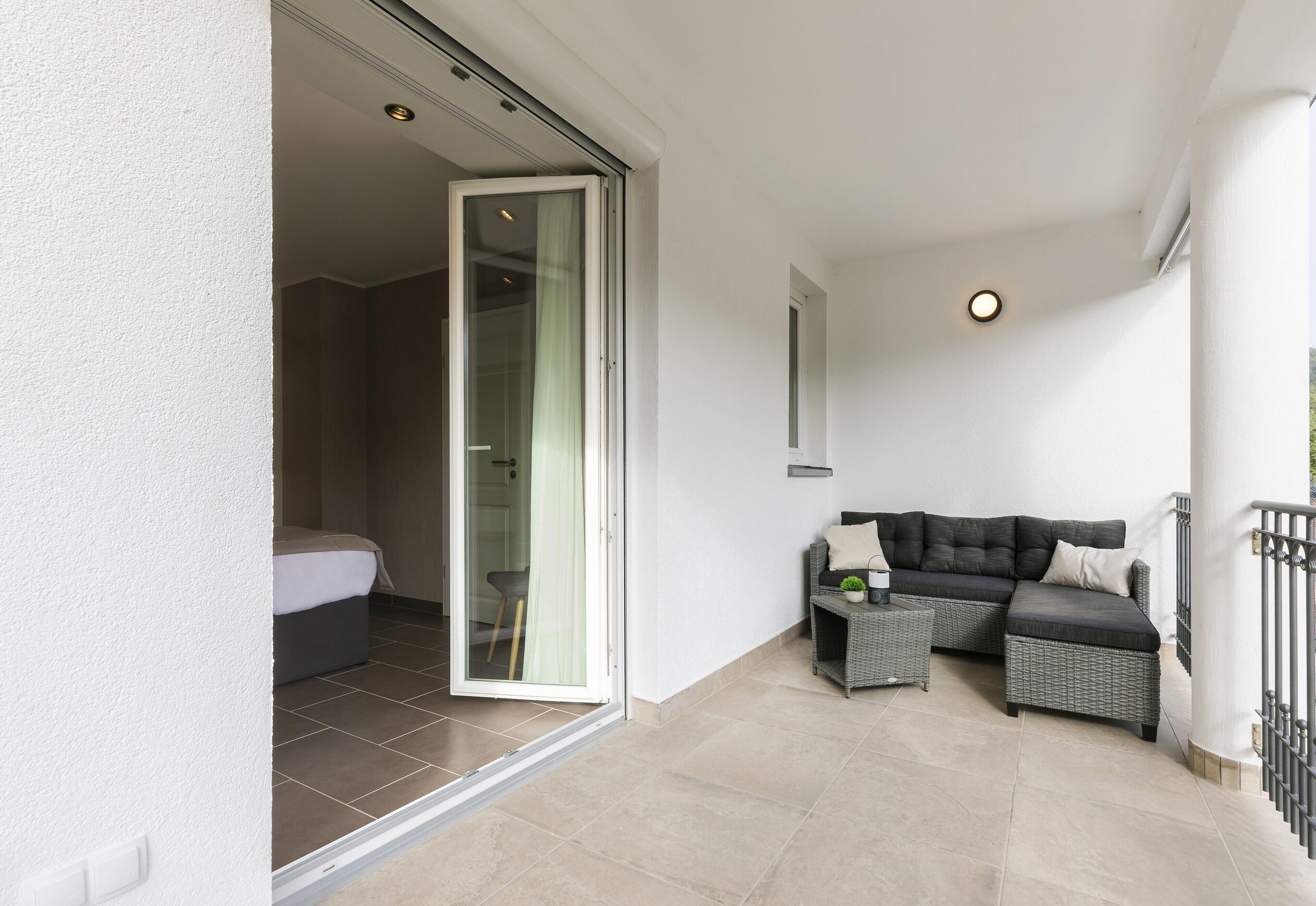 Een balkon met een bank, een klein tafeltje en een schuifdeur naar een slaapkamer.