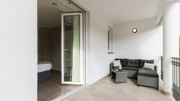 Een balkon met een bank, een klein tafeltje en een schuifdeur naar een slaapkamer.
