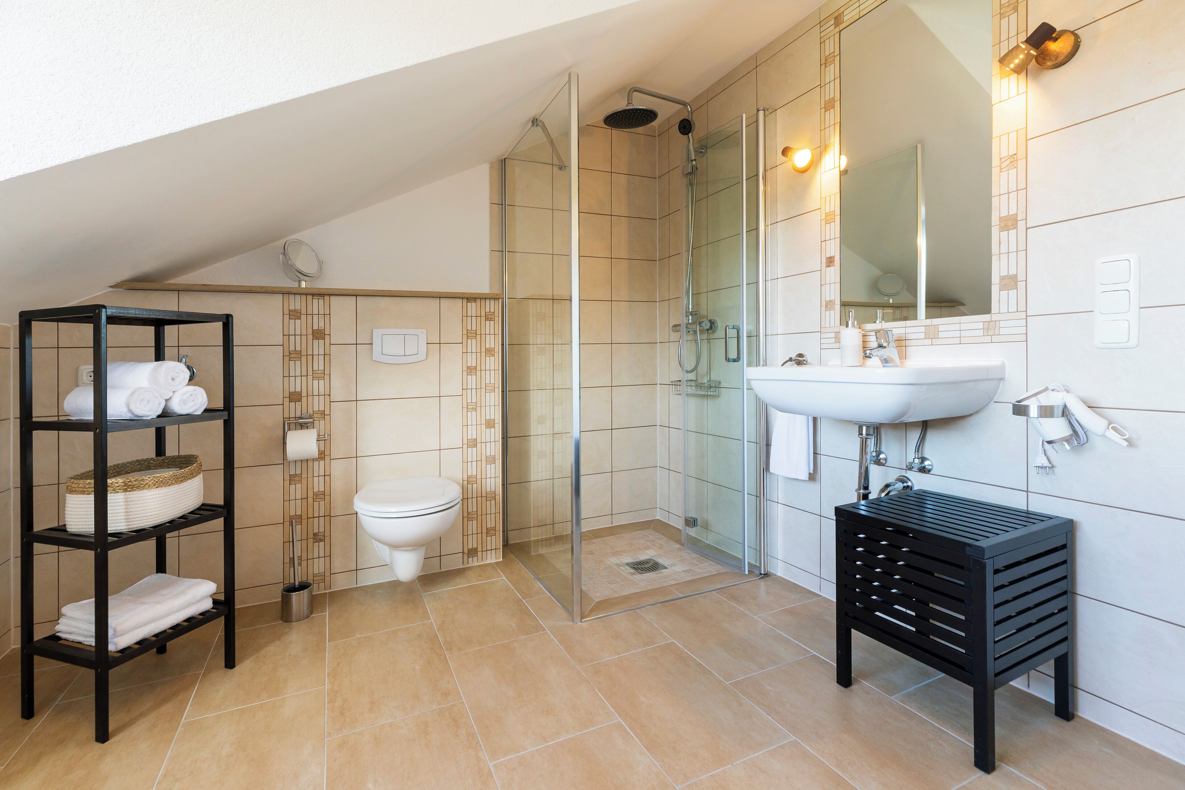 Ein modernes Badezimmer mit einer Glaskabine zur Dusche, einem weißen Waschbecken und einer schwarzen Ablage.