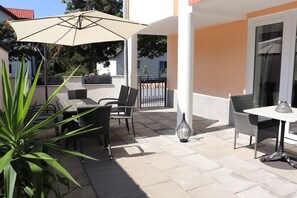 An outdoor patio with wicker furniture, a table, and a large umbrella.