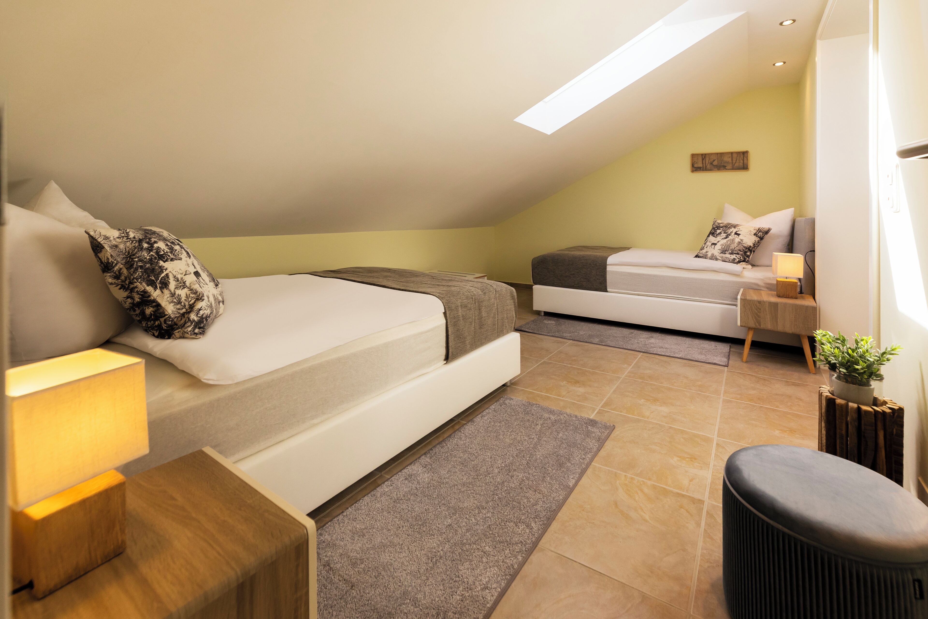 A modern bedroom with two beds, a small seating area, and a skylight.