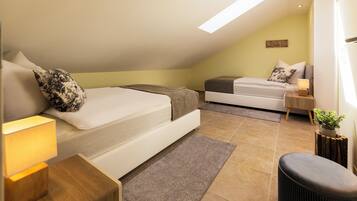 A modern bedroom with two beds, a small seating area, and a skylight.