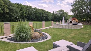A landscaped outdoor area with a stone patio, seating, and a stone fireplace. - Pension Memory (Bischofsheim an der Rhon)