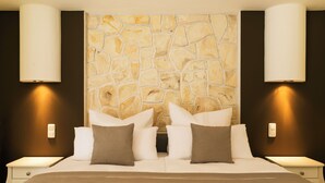 A hotel room with a stone wall headboard, a bed with white and brown bedding, and two bedside tables with lamps. - Pension Memory (Bischofsheim an der Rhon)