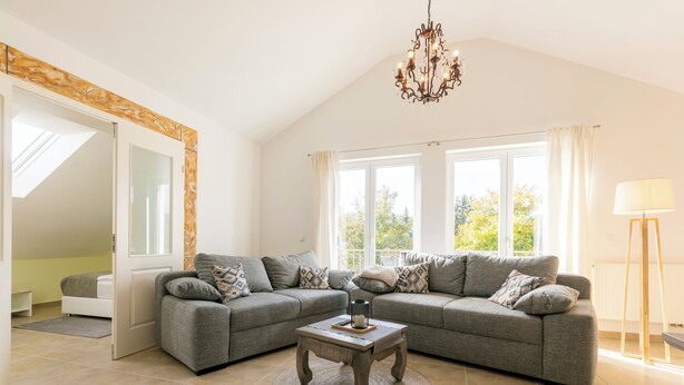 A modern living room with a grey sectional sofa, a round coffee table, and a chandelier. - Pension Memory (Bischofsheim an der Rhon)