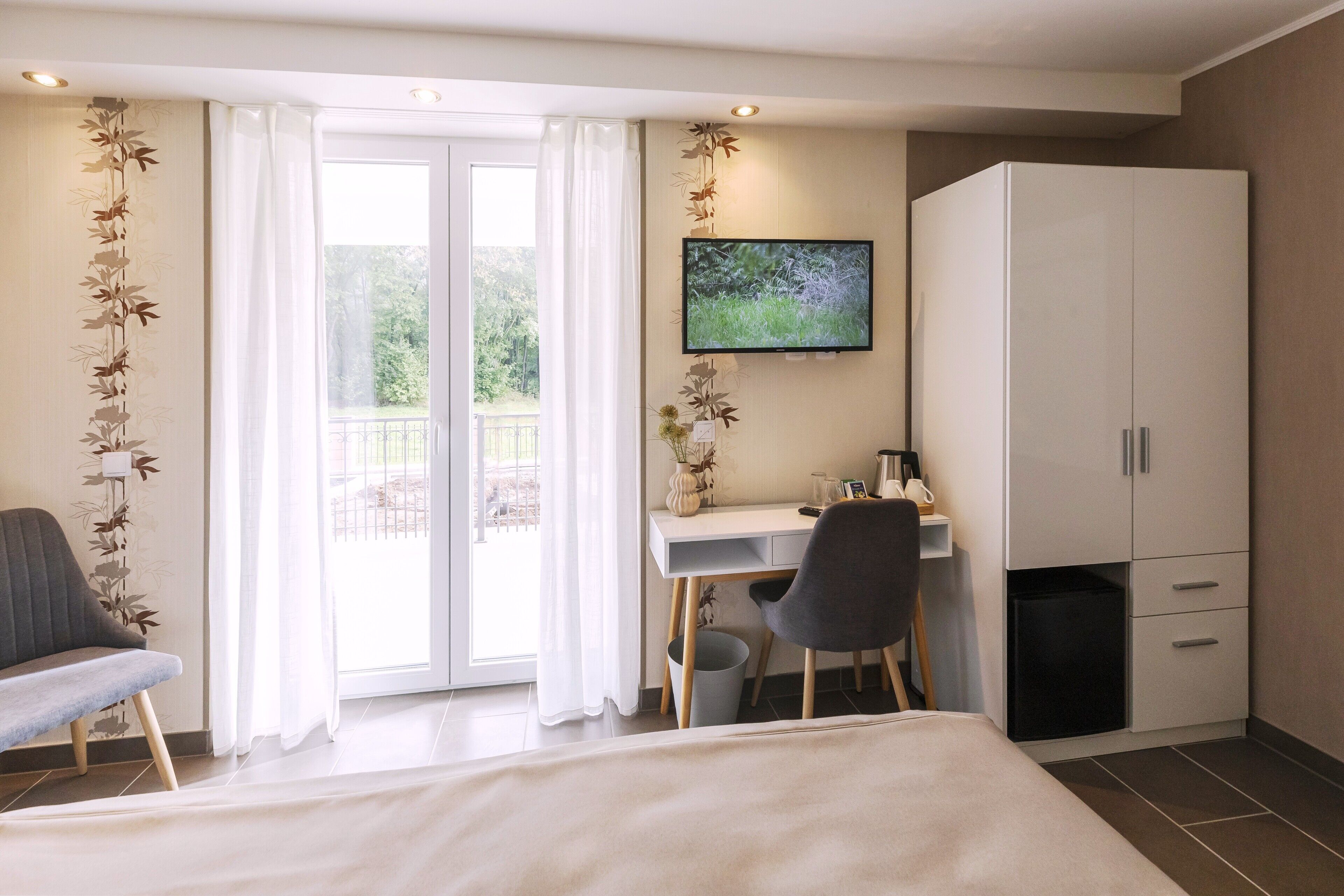 A hotel room with a bed, a desk with a chair, a television, and a wardrobe.