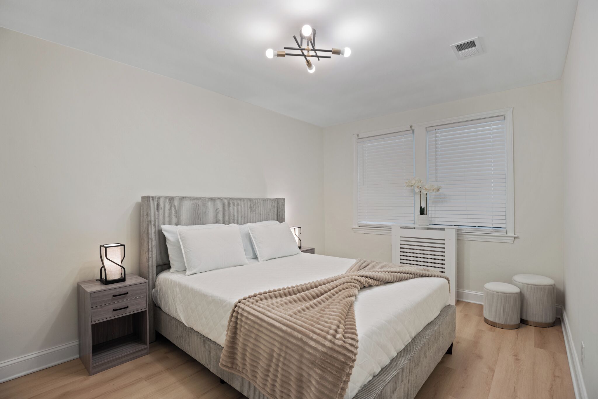 A bedroom with a bed, bedside table, nightstand, and a window with blinds.
