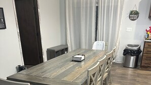 Un espace repas comprenant une longue table en bois, plusieurs chaises, un banc et une poubelle.