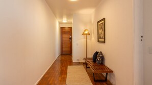 A hallway with wooden flooring, a bench, a lamp, and a door at the end. - 3 Minutes From Leme Beach Gs1102 (Rio de Janeiro)