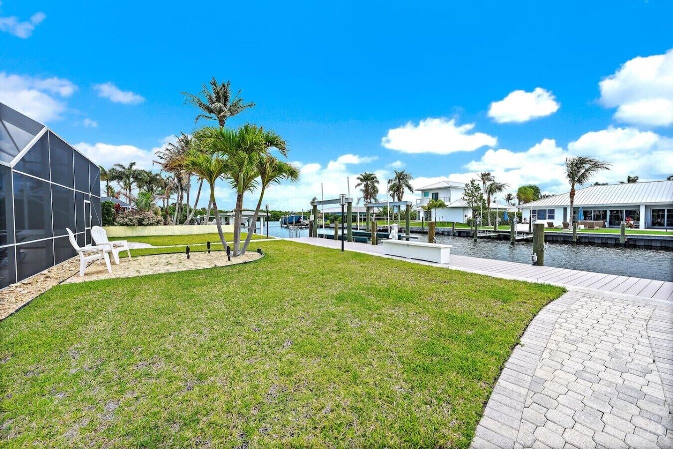 A waterfront property with a grassy lawn, palm trees, a dock, and a modern building with a glass facade.