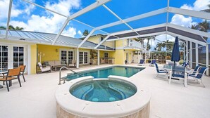 A pool area with a hot tub, lounge chairs, and a covered patio.