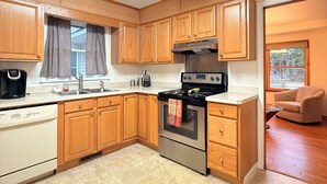 A compact kitchen with wooden cabinets, a stainless steel stove, and a dishwasher. - Poseidon’s Big Getaway – 3BR/2BA Surrounded by Nature, Minutes from the Beach! (Kitty Hawk)