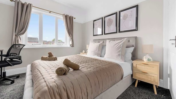 A bedroom with a bed, a desk, a chair, a nightstand, and a window with curtains.