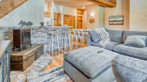 A cozy living room with a stone fireplace, a grey sofa, and a wooden ceiling beam.