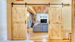 A wooden interior with a sliding barn door leading to a living area with a fireplace, sofa, and TV.