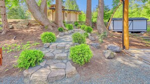 A wooden cabin with a stone pathway leading to it, surrounded by trees and a small shed.