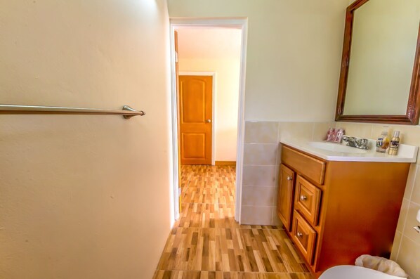 A bathroom with a wooden floor, a white sink, and a mirror above the sink. - Cozy 1-bedroom Studio Apartment in Montserrat with WiFi, and AC (BRADES)