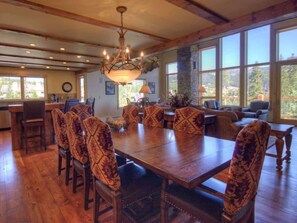 Un comedor amplio con una gran mesa de madera y sillas estampadas, un candelabro y ventanas grandes que ofrecen vistas al exterior.