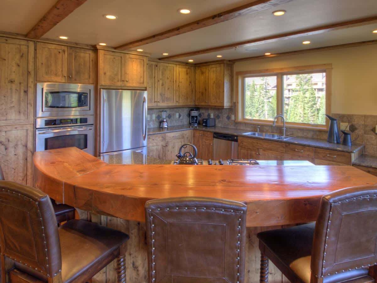 A kitchen with wooden cabinets, stainless steel appliances, and a large island with chairs.