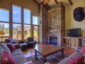 Amplia sala de estar con chimenea de piedra, ventanas grandes y un televisor.