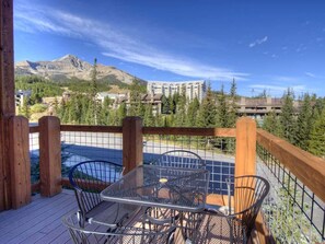 Eine Terrasse mit Tisch und Stühlen, mit Blick auf eine gebirgige Landschaft und ein Gewässer.
