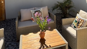 Un espace extérieur accueillant, aménagé avec des meubles en osier, une table en bois et une plante en pot.