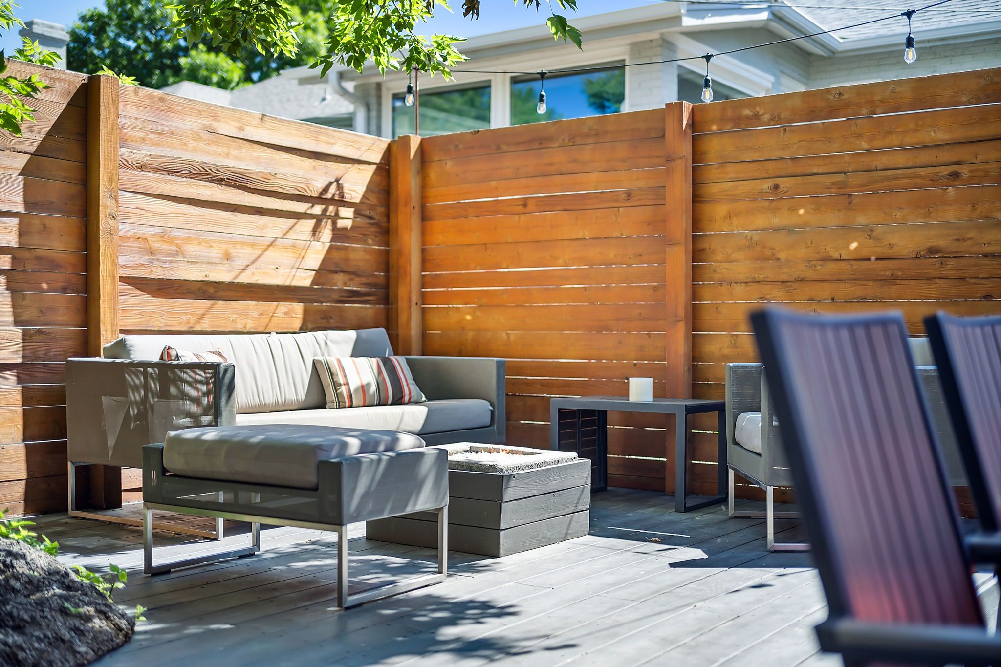 A modern outdoor living space with a wooden deck, a sofa, a coffee table, and a small table with chairs.