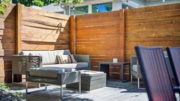 A modern outdoor living space with a wooden deck, a sofa, a coffee table, and a small table with chairs.