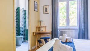 Ein Hotelzimmer mit Bett, Schreibtisch, Stuhl, einem Fenster mit Vorhängen und Blick ins Grüne.
