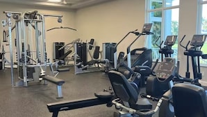 A gym with various exercise machines, a bench, and large windows. - 2-bedroom condo, 5 min to private beach, golf, tiki new pool, hot tub fitness rm (Fort Pierce)