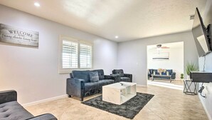 A spacious living room with a grey sofa set, a coffee table, and a TV mounted on the wall.
