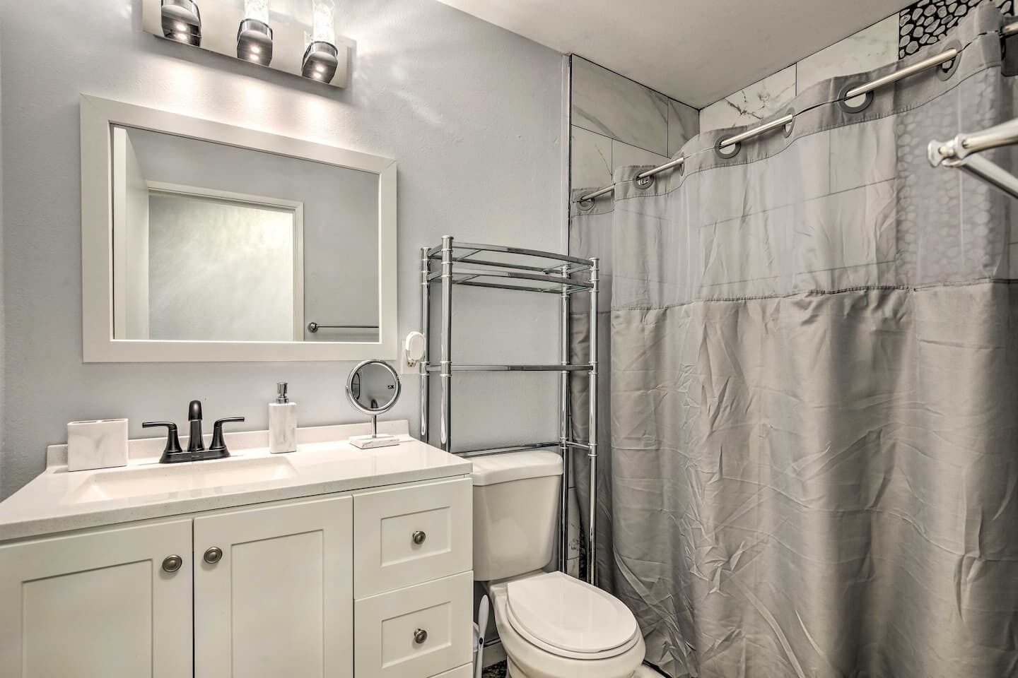 Une salle de bain avec un meuble-lavabo blanc, un miroir, des toilettes et un rideau de douche.