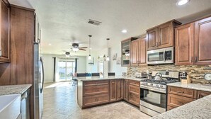 A modern kitchen with wooden cabinets, granite countertops, a stainless steel refrigerator, a microwave, a stove, and a dining area with a view.