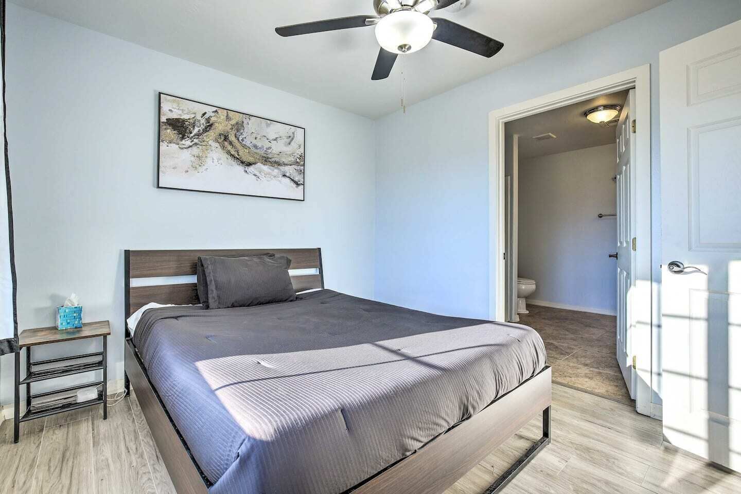 A bedroom with a bed, a nightstand, a ceiling fan, and a door leading to another room.